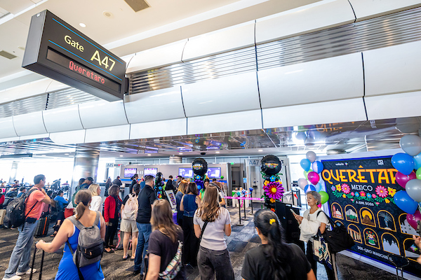 Travelers gather at Gate A47 in an airport terminal, where a festive display celebrates Querétaro, Mexico, with balloons and colorful decorations.